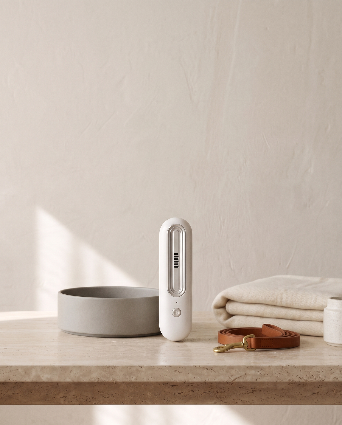 White OzoFreshen device on a travertine table beside a ceramic pet bowl, leather leash and folded blanket